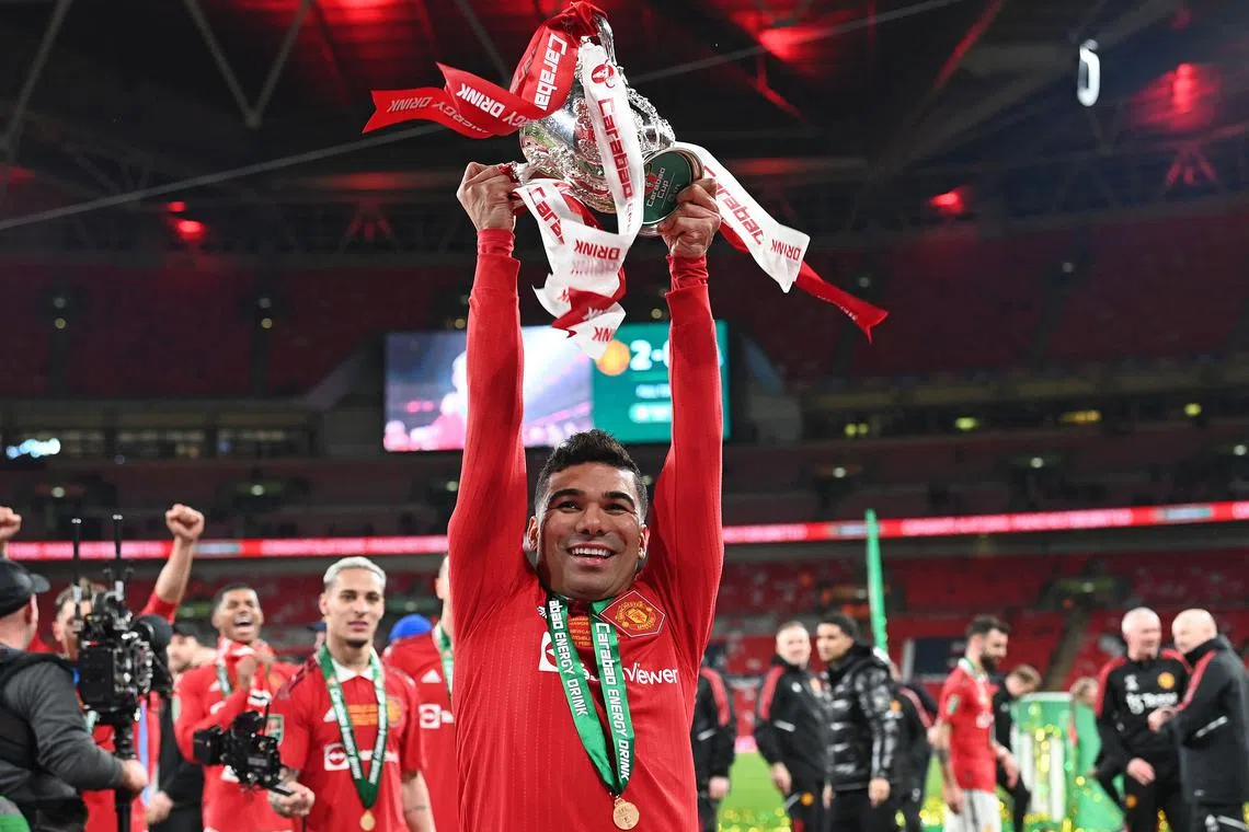 Manchester United's Brazilian midfielder Casemiro holds the trophy as Manchester United players celebrate their win.