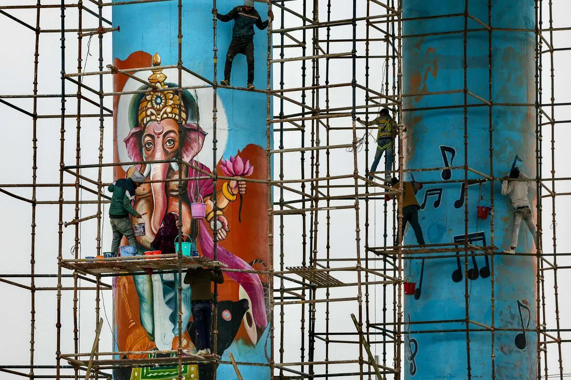 Workers paint a mural of elephant-headed Hindu deity Ganesha on a pillar, ahead of the Maha Kumbh Mela festival in Prayagraj.