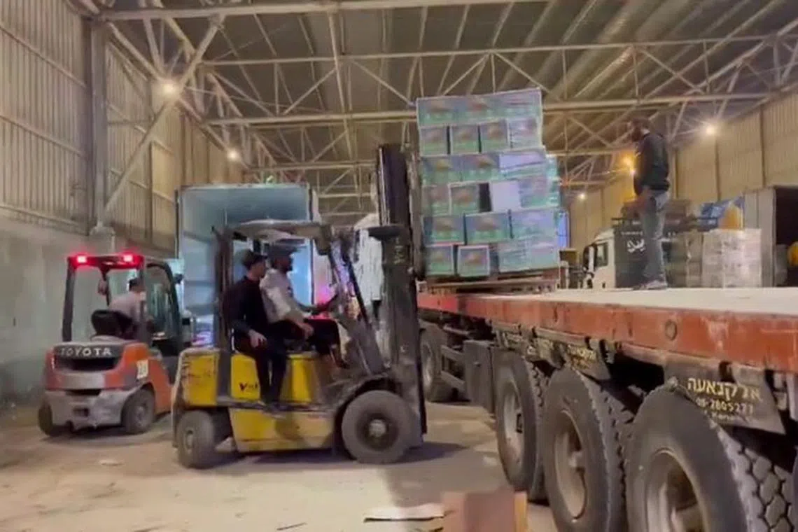 Aid and relief assistance materials are unloaded from trucks, amid the ongoing conflict between Israel and the Palestinian Islamist group Hamas, at a location given as Rafah border crossing, in this screen grab obtained from video released December 7, 2023.     Palestine Red Crescent Society/Handout via REUTERS