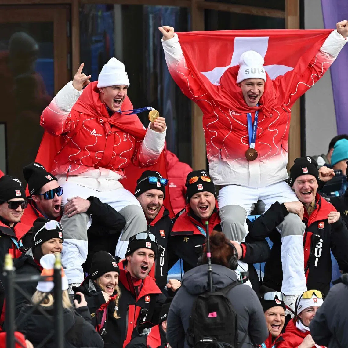 Gold medallist Franjo von Allmen (left) and bronze medallist Marco Odermatt, both of Switzerland, celebrating with team members after the men's super-G alpine skiing event during the 2026 Milano- Cortina Winter Olympic Games at the Stelvio Ski Centre in Bormio on Feb 11, 2026.