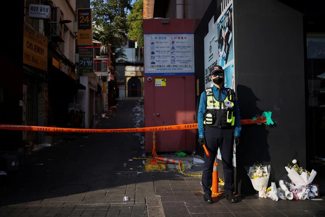 A police officer stands guard near floral tributes at the scene of a crowd crush that happened during Halloween festivities, in Seoul, South Korea, Nov 1, 2022. 