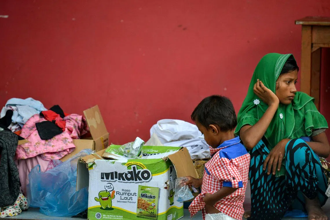 A Rohingya refugee sits next to clothes donated by villagers at a temporary shelter following their arrival by boat in Laweueng, Aceh province on December 27, 2022.  