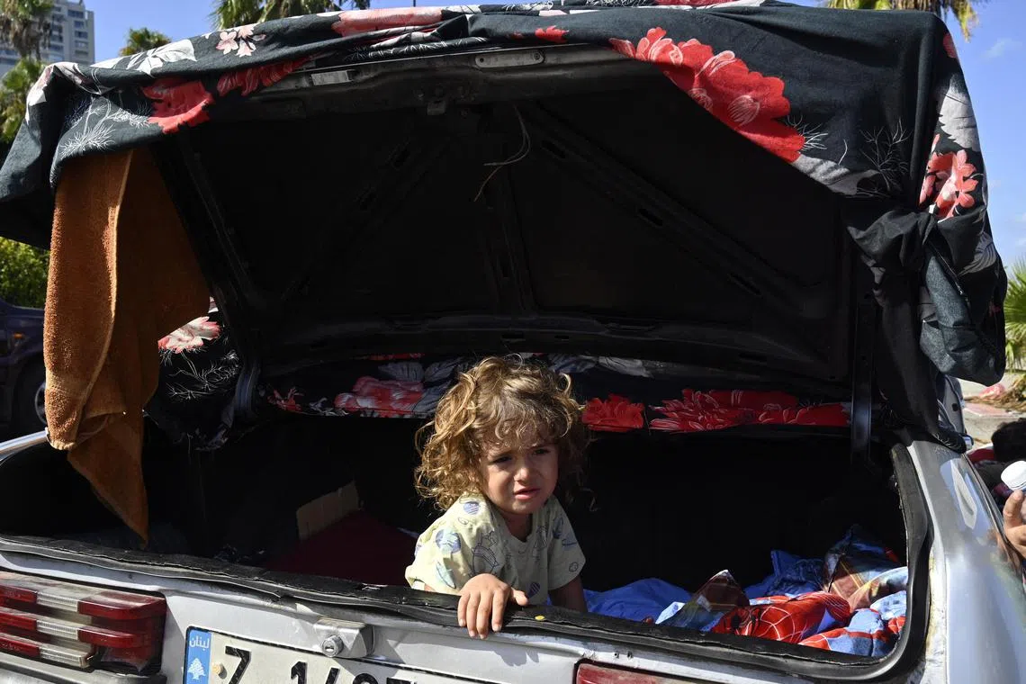 A child displaced by a devastating war between Israel and Hezbollah sleeps in the trunk of a car parked along a street in Beirut.