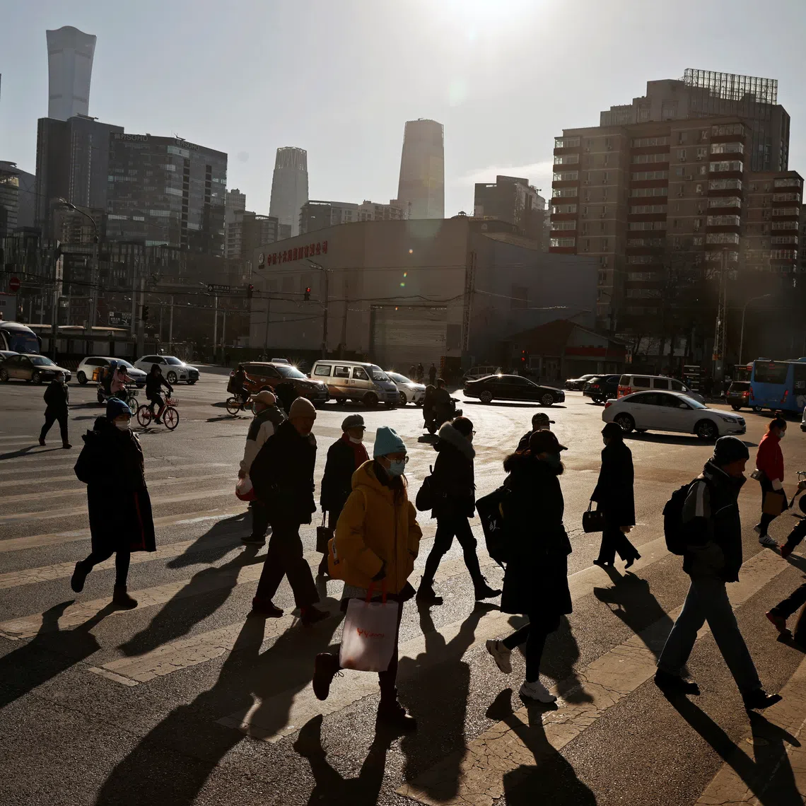 People cross a street during morning rush hour in front of the skyline of the central business district (CBD) in Beijing, China December 15, 2020. REUTERS/Thomas Peter