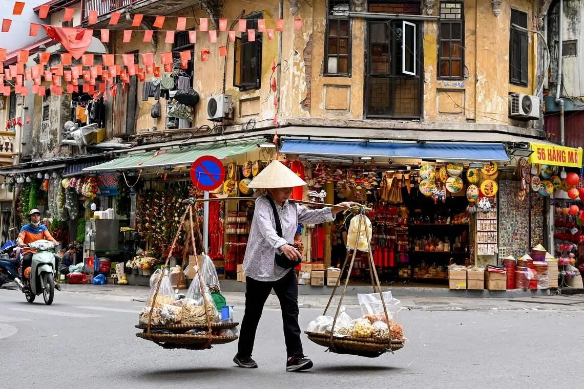 TOPSHOT - A street vendor walks down a street carrying food for sale in Hanoi on April 21, 2026. (Photo by Nhac NGUYEN / AFP)