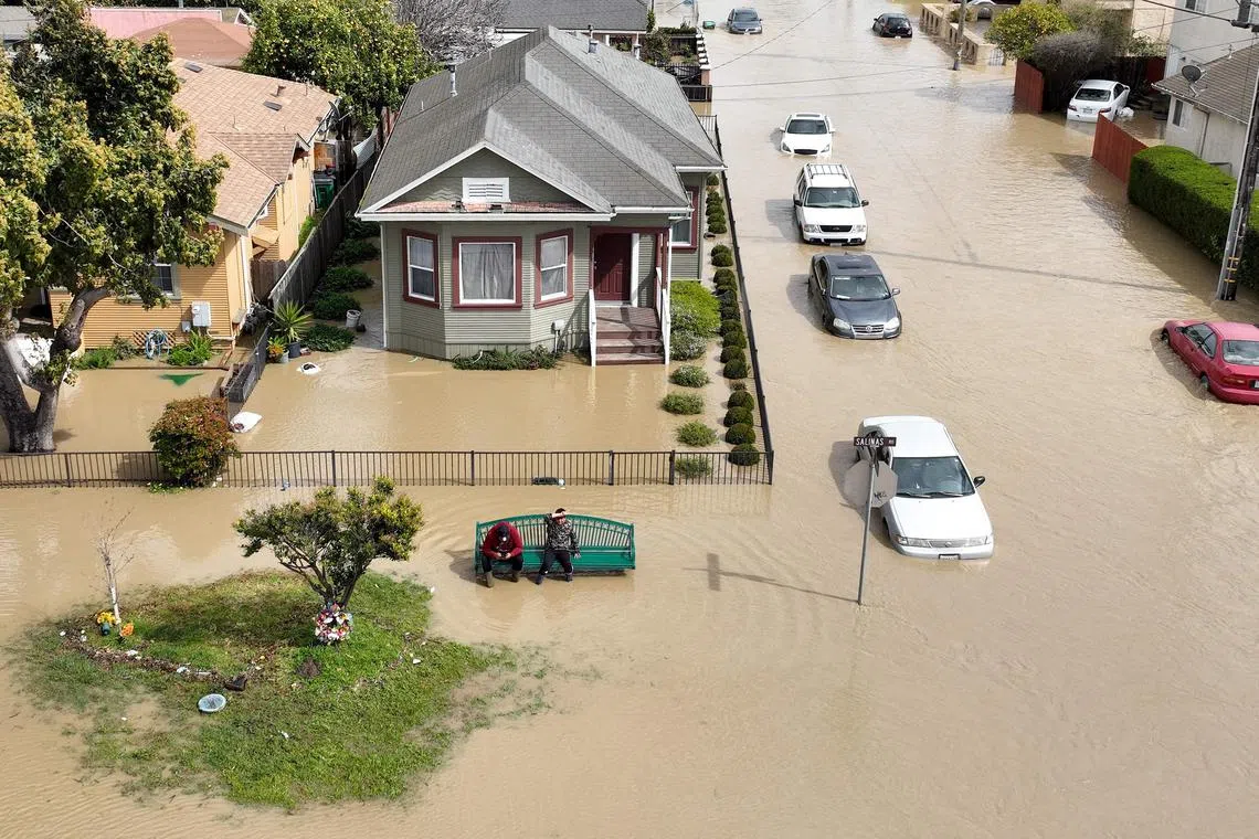 An aerial view shows people sitting on a bench in a flooded neighbourhood of Pajaro in Watsonville, California, on March 11, 2023.  Residents were forced to evacuate in the middle of the night after an atmospheric river surge broke the Pajaro Levee and sent flood waters flowing into the community. 