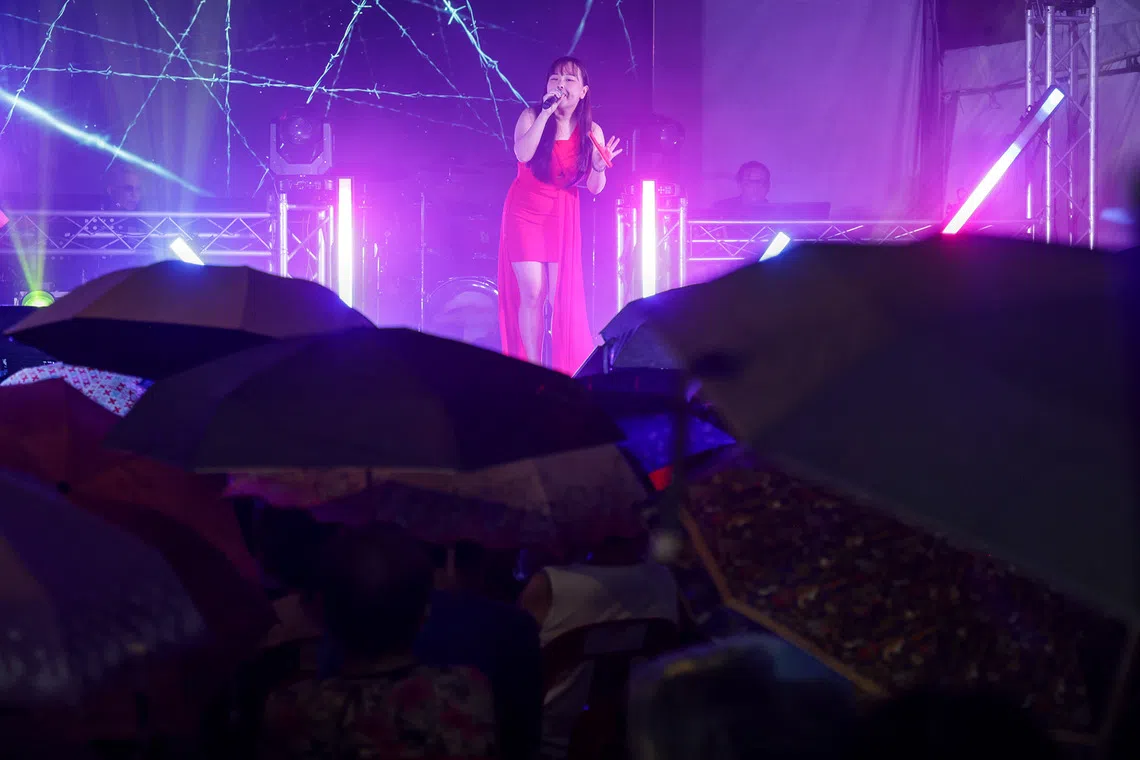 ST20260816_202670800792/Jasel Poh/sfghost/

A getai singer performing in the rain as audience members shelter under umbrellas during the getai show held at Block 408 Ang Mo Kio Avenue 10 on Aug 16, 2026.
