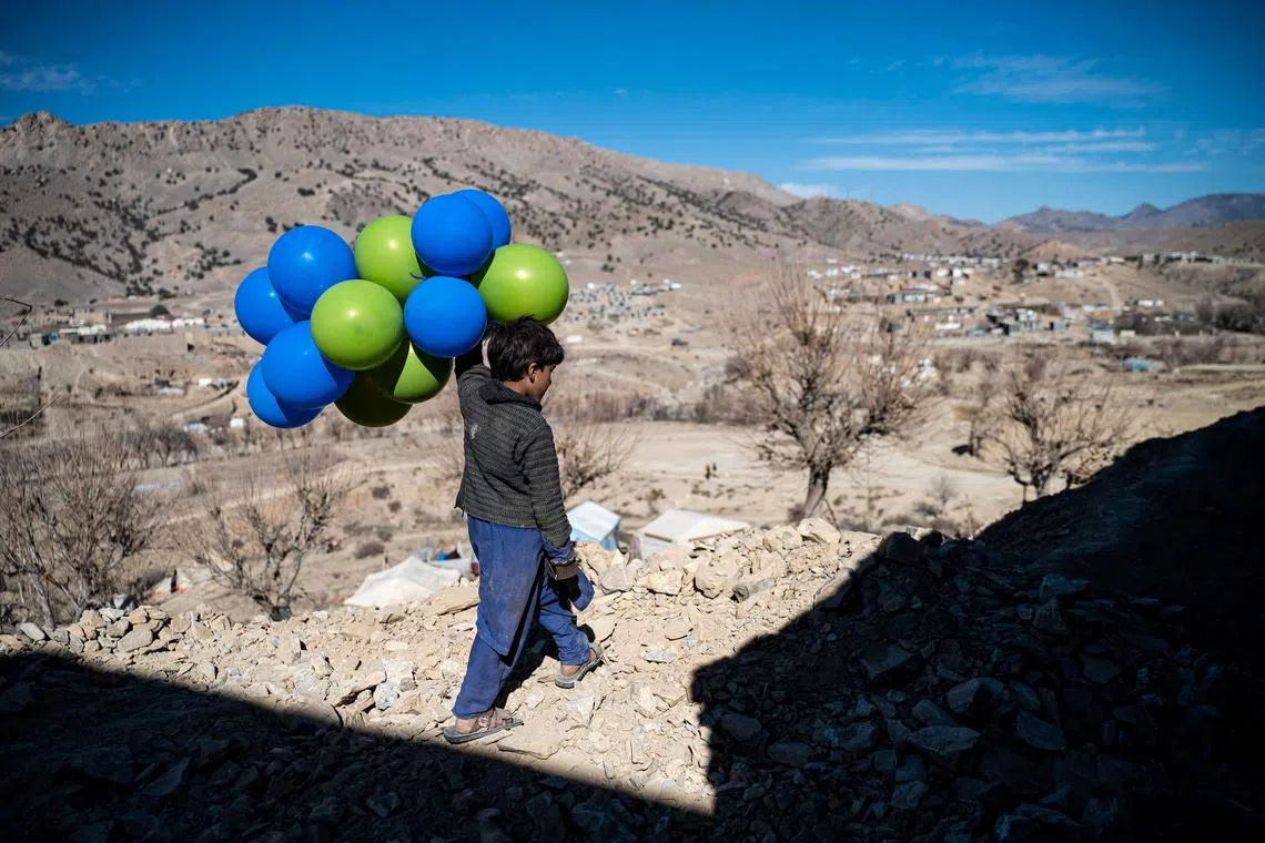 An Afghan boy holds balloons as he walks downhill along a path in Barmal district of Paktika province on December 15, 2022.
