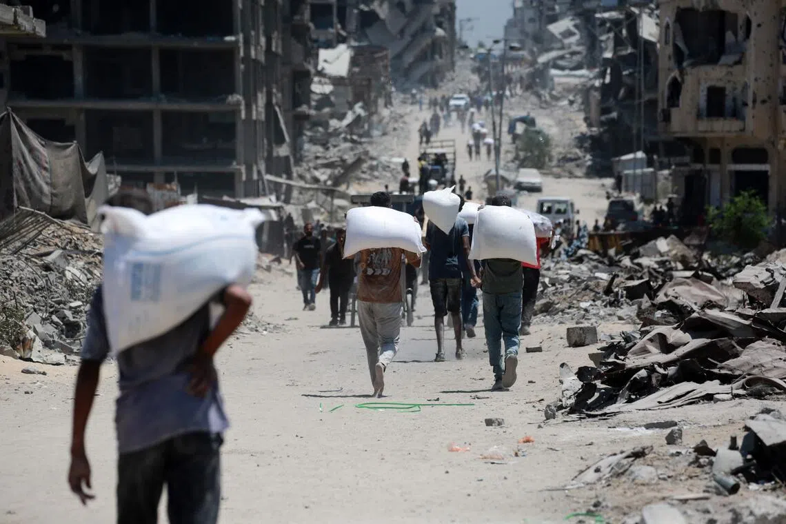 Palestinians carry bags of flour that they obtained from aid trucks.