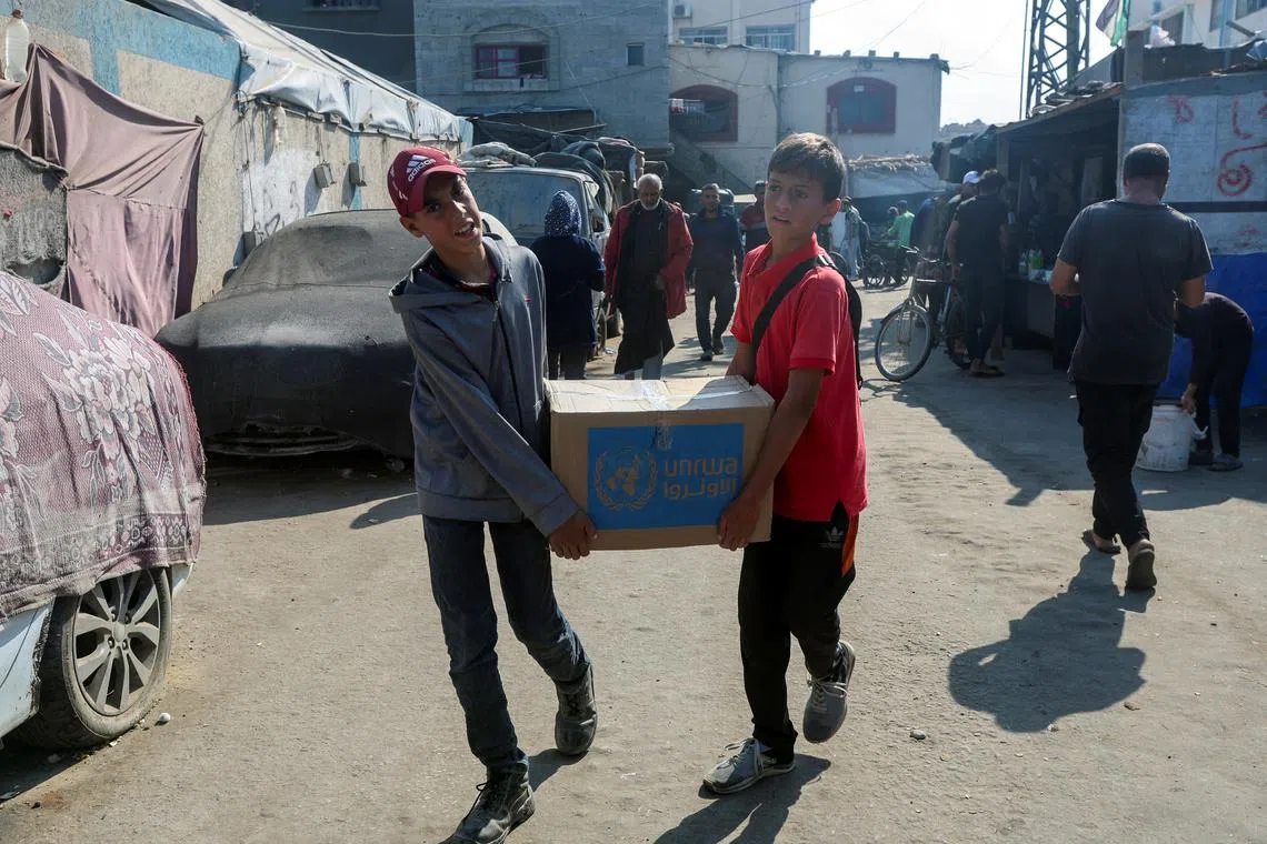 Palestinians carry an aid box distributed by the United Nations Relief and Works Agency (UNRWA), amid the Israel-Hamas conflict, in Deir Al-Balah, central Gaza Strip, November 4, 2024. REUTERS/Ramadan Abed