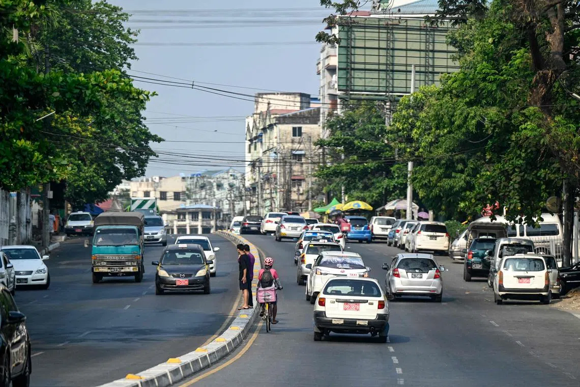 A delivery man (C) rides his bicycle between cars along a road during a heatwave in Yangon on April 29, 2024. Delivery riders pedal their bicycle through a punishing heatwave in Myanmar's commercial capital Yangon, where scooters and motorbikes are banned. (Photo by Sai Aung MAIN / AFP) / TO GO WITH "MYANMAR-HEAT-WEATHER"
