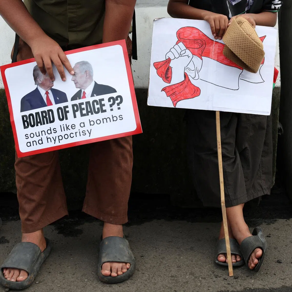 Boys in solidarity with Palestinians hold signs as they take part in a protest, outside the U.S. embassy, against Israel and demanding that the Indonesian government cancel the proposed multinational peacekeeping force for Gaza, following  Indonesia's President Prabowo Subianto invitation to Washington later this month for the first meeting of U.S. President Donald Trump's Board of Peace, in Jakarta, Indonesia, February 13, 2026. REUTERS/Ajeng Dinar Ulfiana