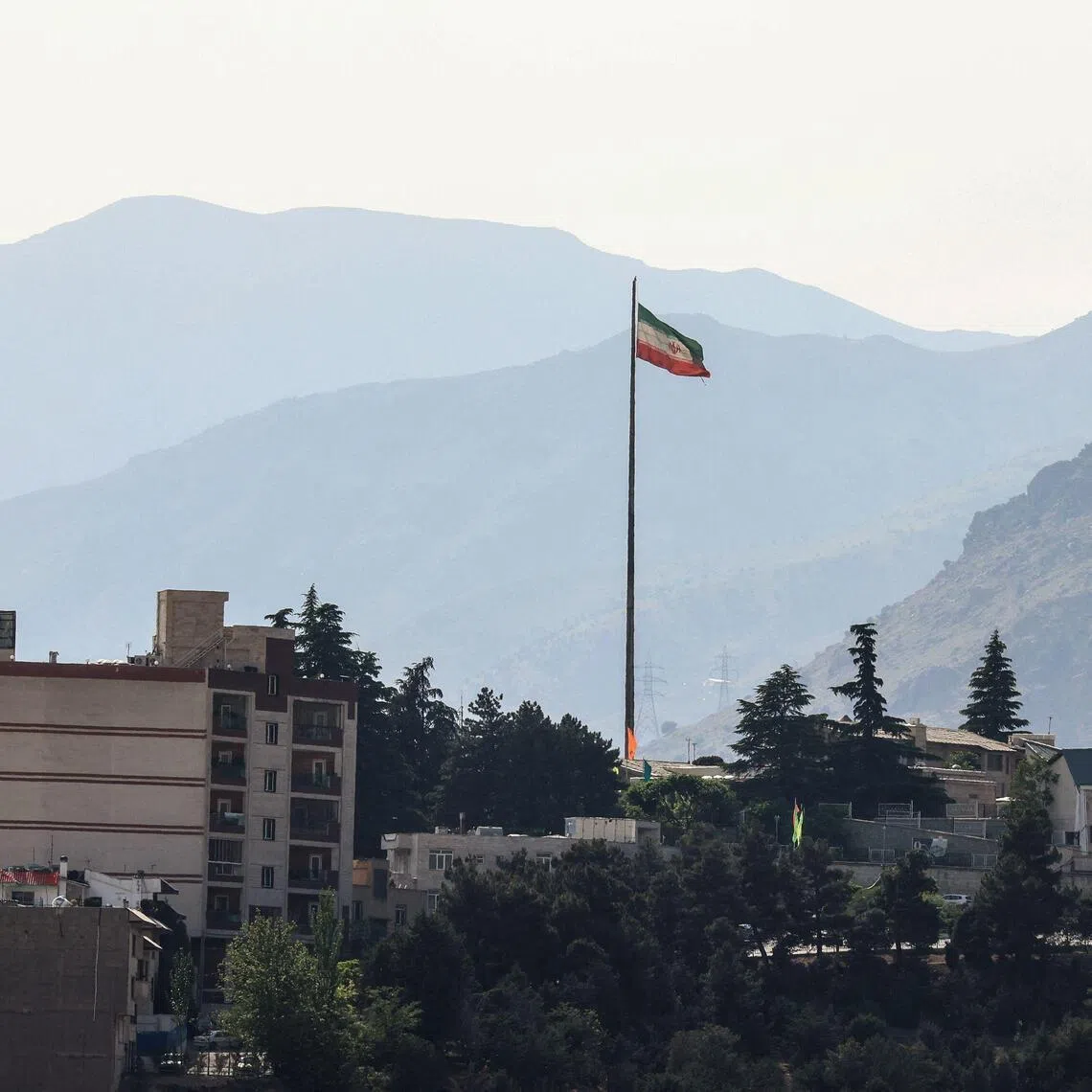 The Iran flag flutters from a tall flagpole over high-rise buildings in northern Tehran on May 12, 2026. Iran's chief negotiator said May 12, that Washington must accept Tehran's latest peace plan or face failure, after US President Donald Trump warned the truce in the Middle East war was on the brink of collapse. (Photo by ATTA KENARE / AFP) / 