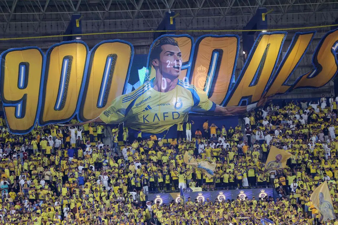 Al Nassr supporters cheer in the stands beneath a large banner depicting their Portuguese forward Cristiano Ronaldo ahead of the Saudi Pro League match against Al-Ahli.