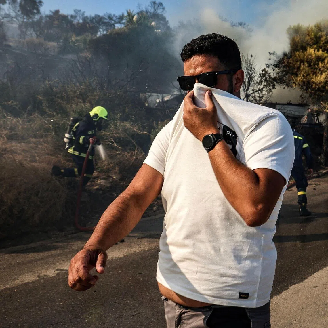 A man covering his face from the smoke as firefighters tackle a wildfire on the island of Salamina, near Athens, on Aug 16.