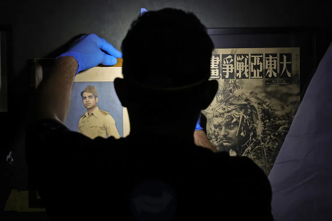 An art handler aligning artifacts from the Indian National Army (INA) — a photograph of Captain John Jacob (left) and a wartime paraphernalia (right) — using pencils and rulers for precise spacing in the Fall of the Fortress section of the gallery on Aug 20, 2026. Formed during the Japanese invasion of Malaya and Singapore, the INA comprised British Indian Army prisoners-of-war who fought for India’s independence.