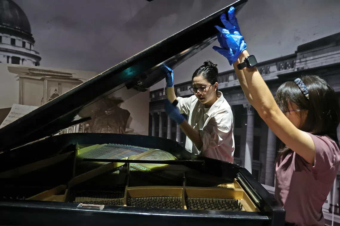(From right) Kong Yen Lin, assistant curator, National Museum of Singapore, and Lee Sang Hee, assistant conservator (Organic Objects), Heritage Conservation Centre, conducting visual checks on Zubir Said's piano after it was shifted into position in the Towards a New Identity section of the gallery on July 21, 2026.