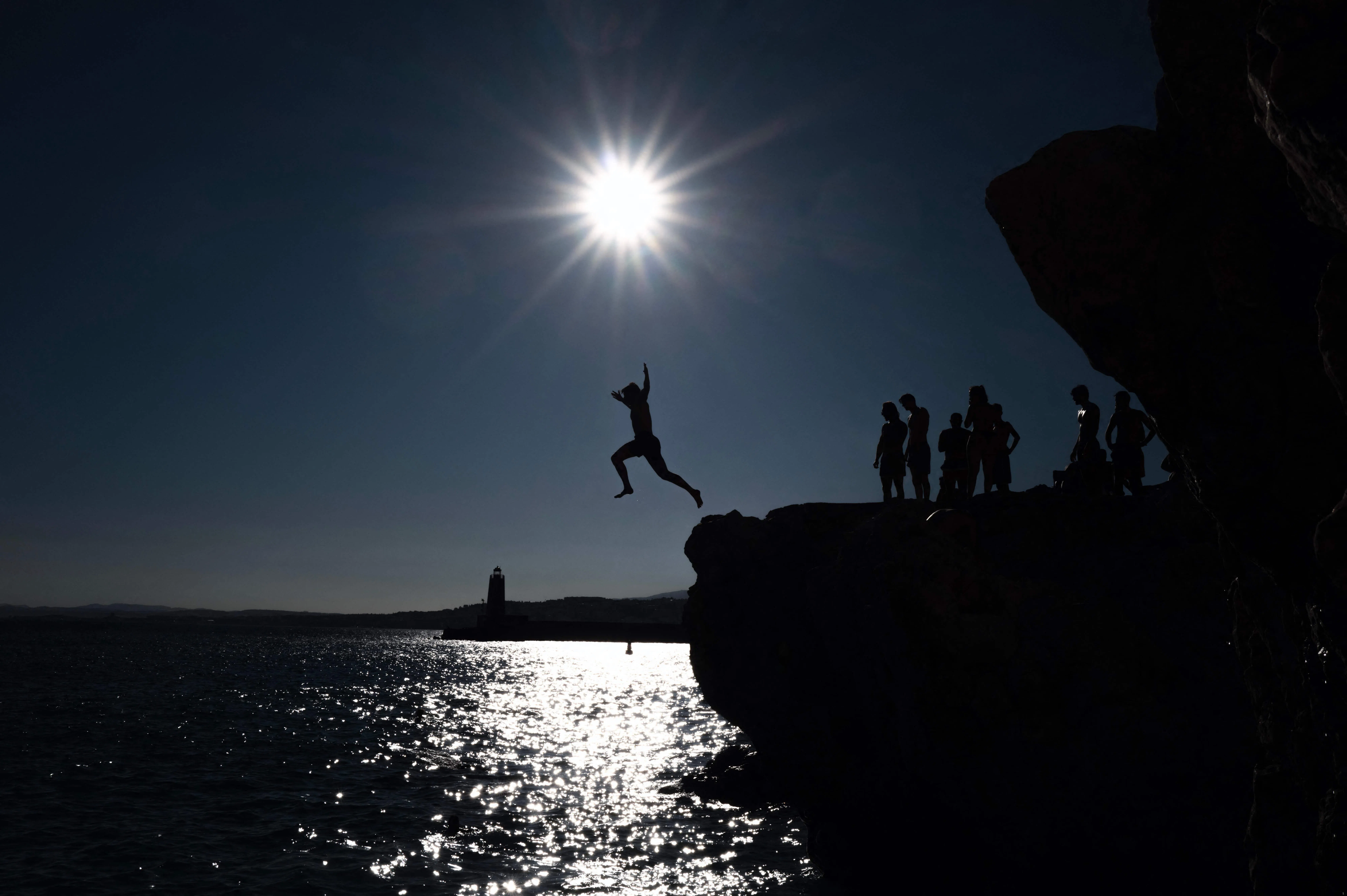 TOPSHOT - A silhouetted person jumps from a rocky seaside into the Mediterranean sea on a sunny day in the French riviera city of Nice, south-eastern France, on August 22, 2026. (Photo by Valery HACHE / AFP)