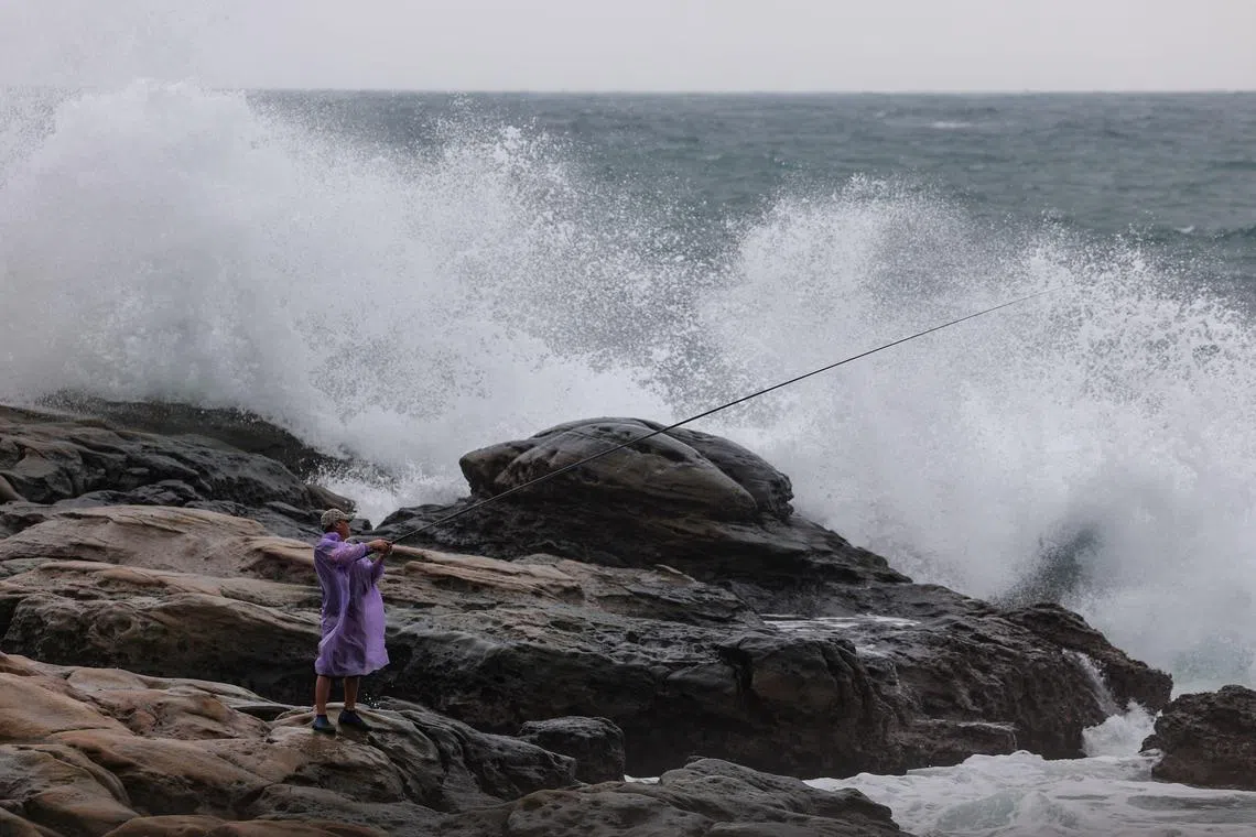 A fisherman holds a fishing rod next to waves as Typhoon Kong-rey approaches, in Keelung on October 29, 2024. 