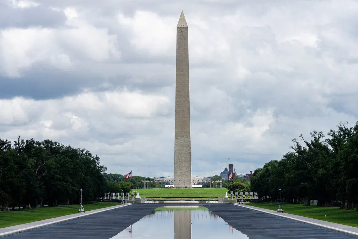 A tall obelisk stands in a large, open plaza with surrounding trees.