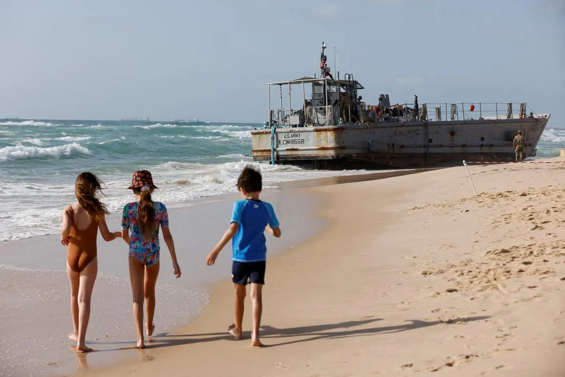 Israeli children walking along the shore near one of four beached vessels used for delivering aid to Palestinians in Gaza.