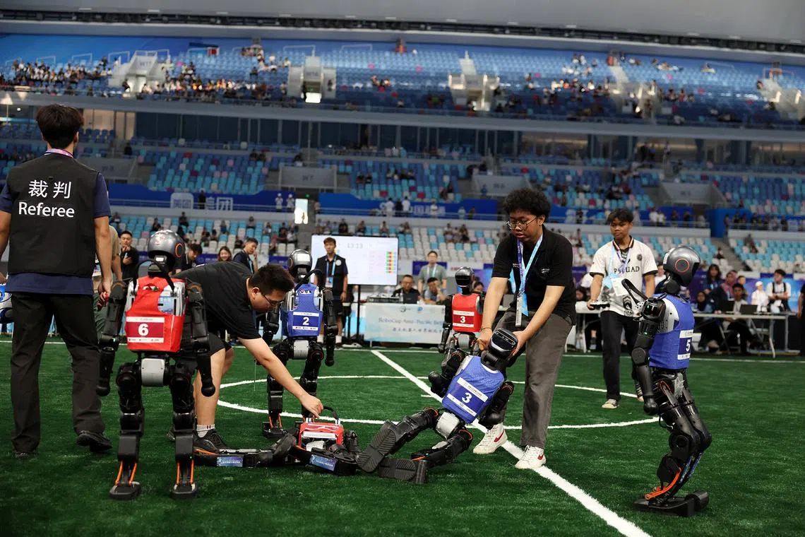People moving fallen Booster Robotics T1 humanoid robots during a 5-on-5 soccer group match at the inaugural World Humanoid Robot Games, at the National Speed Skating Oval in Beijing, China, on Aug 15.