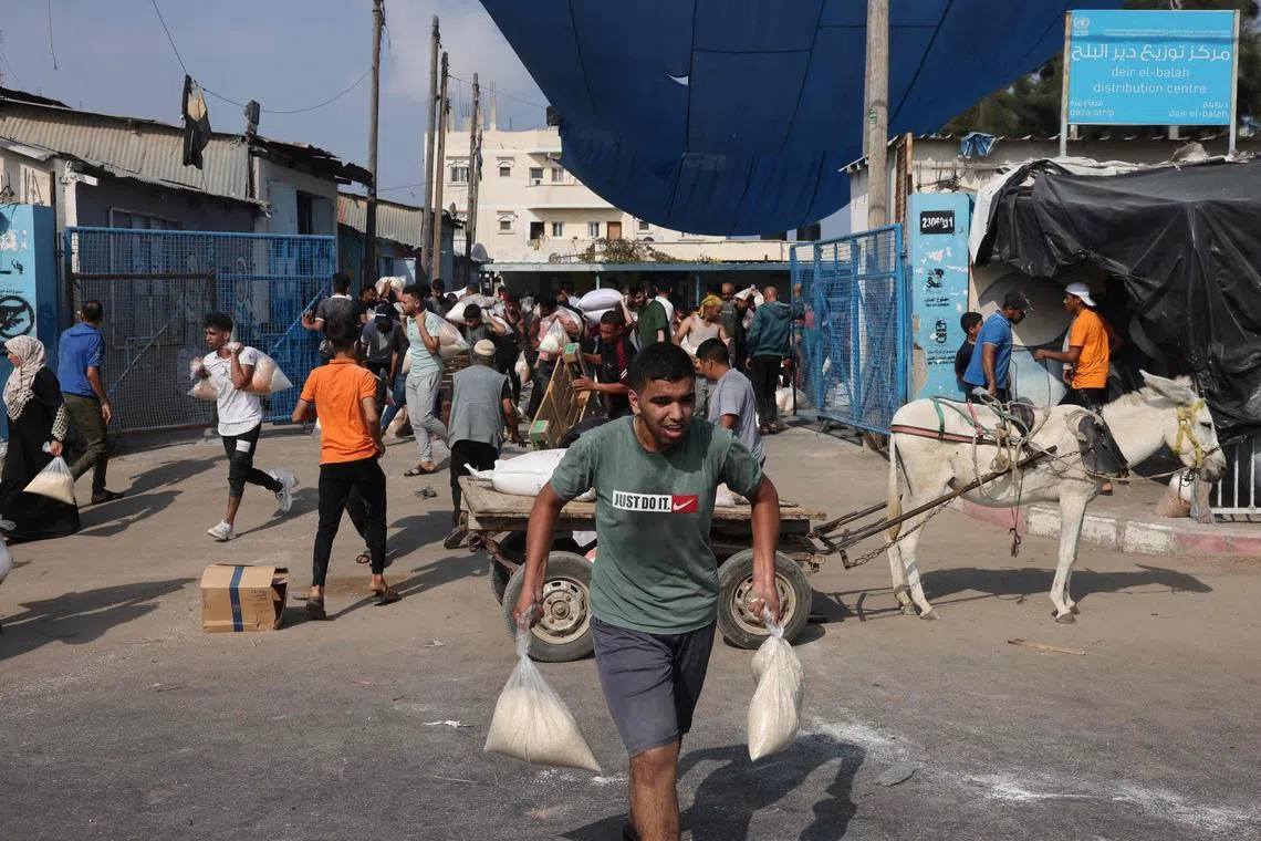 Palestinians collect bags of dried pulses from a UN-run aid supply center, distributing food to local Palestinians and people displaced following Israel's call for more than 1 million residents in northern Gaza to move south for their safety, in Deir al-Balah on October 28, 2023, amid the ongoing battles between Israel and the Palestinian group Hamas. Thousands of civilians, both Palestinians and Israelis, have died since October 7, 2023, after Palestinian Hamas militants based in the Gaza Strip entered southern Israel in an unprecedented attack triggering a war declared by Israel on Hamas with retaliatory bombings on Gaza. (Photo by MOHAMMED ABED / AFP)
