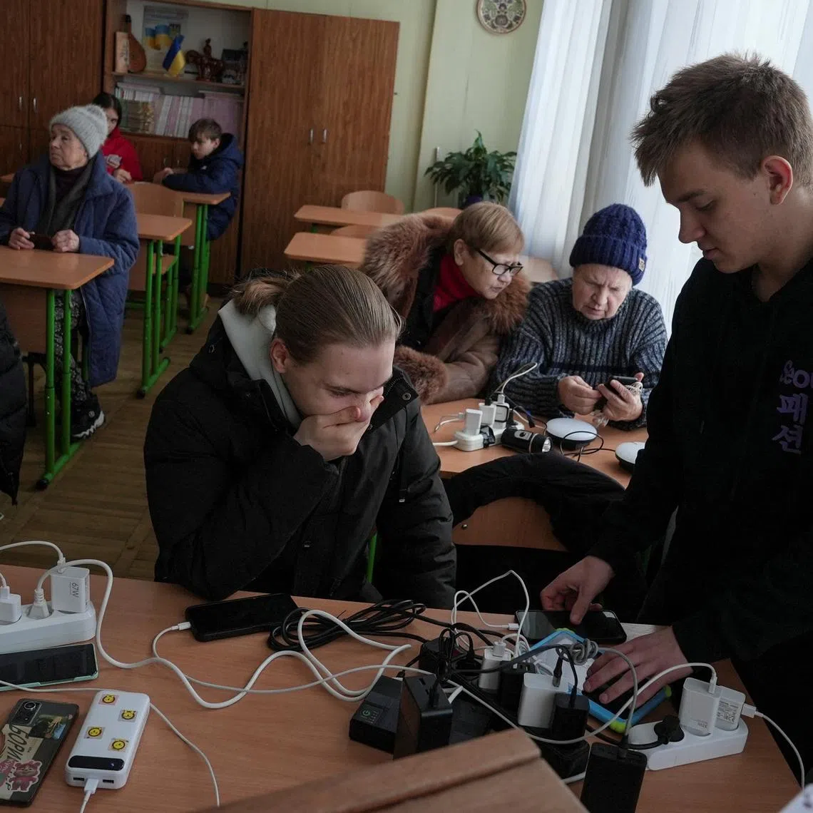 Residents wait while charging their devices inside a school classroom turned into a humanitarian aid point during a power blackout after critical civil infrastructure was hit by recent Russian missile and drone strikes, amid Russia's attack on Ukraine, in Kyiv, Ukraine January 11, 2026. REUTERS/Anna Voitenko