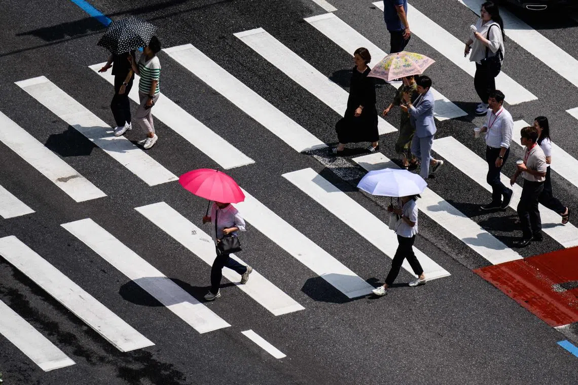Pedestrians use umbrellas for shade as they cross a road in Seoul on Aug 14.