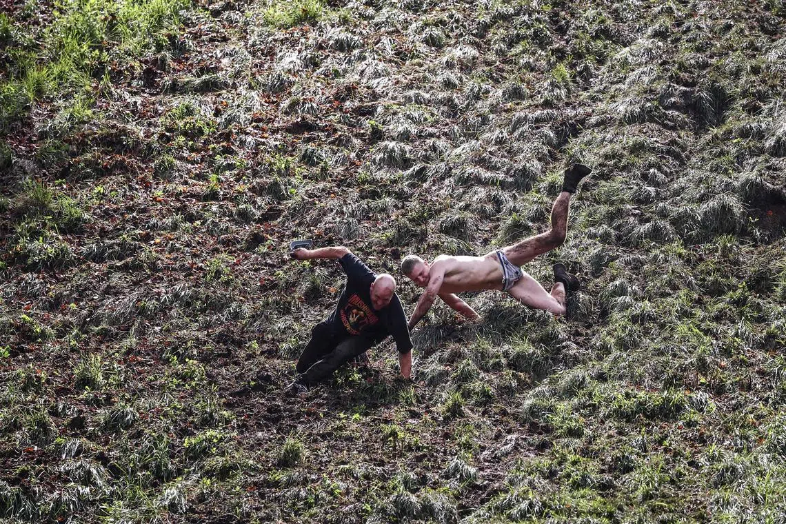 Competitors come tumbling down the hill in pursuit of a round Double Gloucester cheese during the annual Cooper's Hill cheese rolling competition near the village of Brockworth, Gloucester, in western England, on May 27, 2024. The annual Cooper's Hill Cheese Rolling involves competitors chasing an eight pound Double Gloucester cheese down a steep hill. 