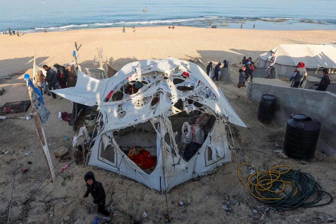 A Palestinian boy stands next to a damaged tent for displaced people at the site of an Israeli strike on a beachfront cafe, amid the ongoing conflict between Israel and Hamas, in Deir Al-Balah in the central Gaza Strip, January 14, 2025. REUTERS/Ramadan Abed      TPX IMAGES OF THE DAY     