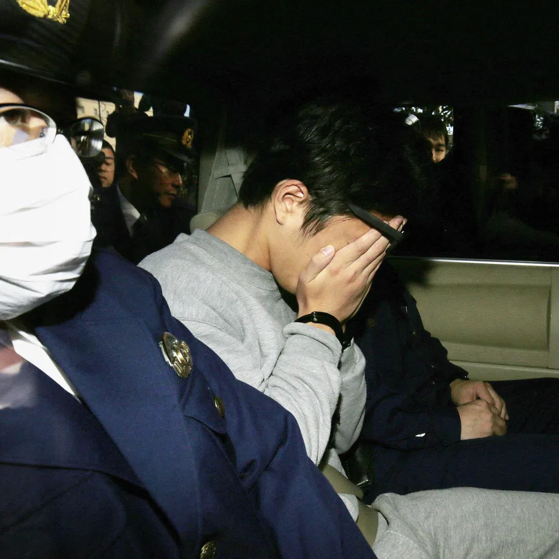 Suspect Takahiro Shiraishi (C) covers his face with his hands as he is transported to the prosecutor's office from a police station in Tokyo on November 1, 2017. The 27-year-old Japanese man, who was arrested after police found nine dismembered corpses rotting in his house, has confessed to killing all his victims over a two-month spree after contacting them via Twitter, media reports. (Photo by JIJI PRESS / AFP) / Japan OUT
