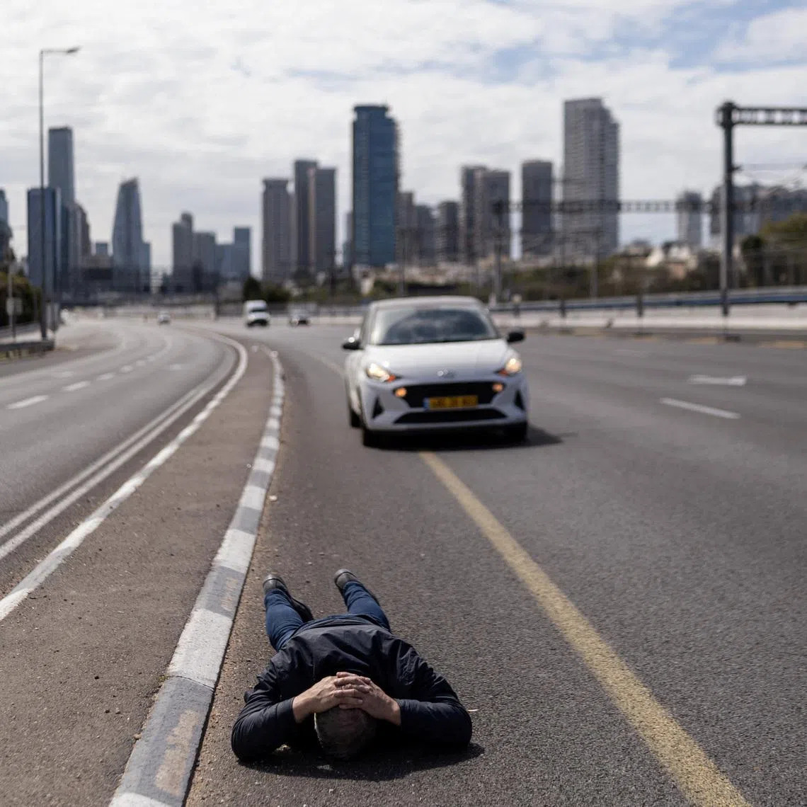 A man lies on the road to take cover as an air raid siren sounds following a barrage of missiles from Iran, amid the US-Israel conflict with Iran, in central Israel, March 9, 2026.