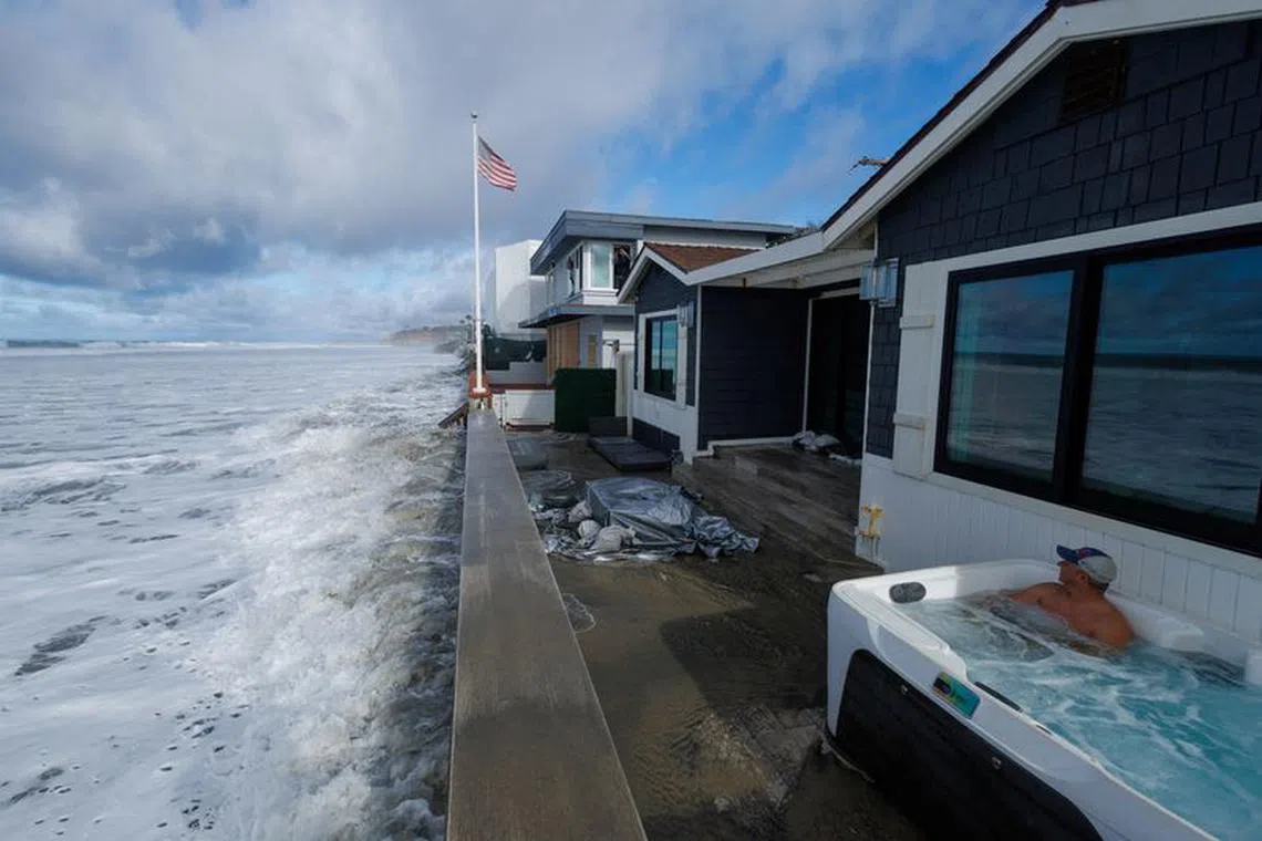 Andy Grubbs, of Virginia, watches from a hot tub as large ocean swells combining with a high tide allows waves to reach beachfront homes in Del Mar, California, U.S., December 30, 2023.  REUTERS/Mike Blake