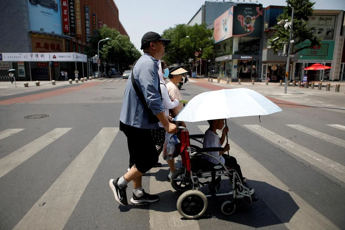FILE PHOTO: Pedestrians cross a road on a hot day amid an orange alert for heatwave, in Beijing, China June 16, 2023. REUTERS/Florence Lo/File Photo
