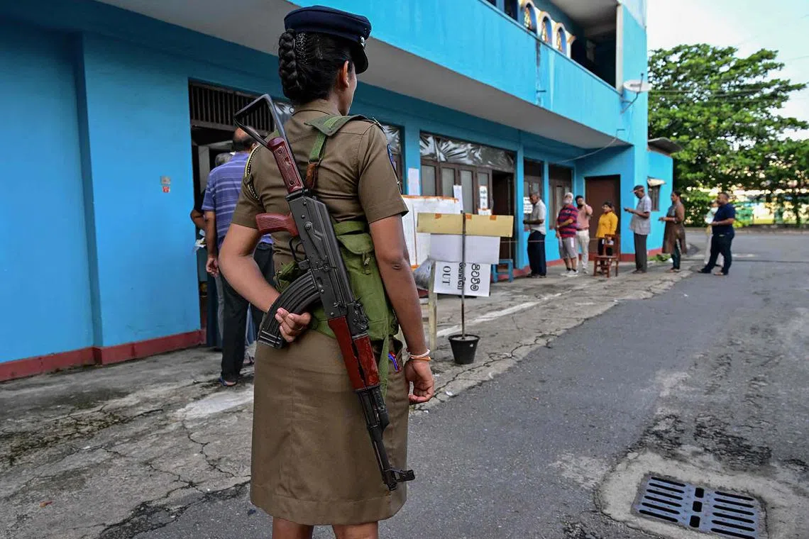 TOPSHOT - A policewoman keeps watch at a polling station as people queue before casting their ballots to vote in Sri Lanka's parliamentary election in Colombo on November 14, 2024. Polls opened in Sri Lanka's parliamentary vote on November 14, AFP journalists saw, the island's first election under President Anura Kumara Dissanayake, who came to power two months ago. (Photo by Ishara S. KODIKARA / AFP)