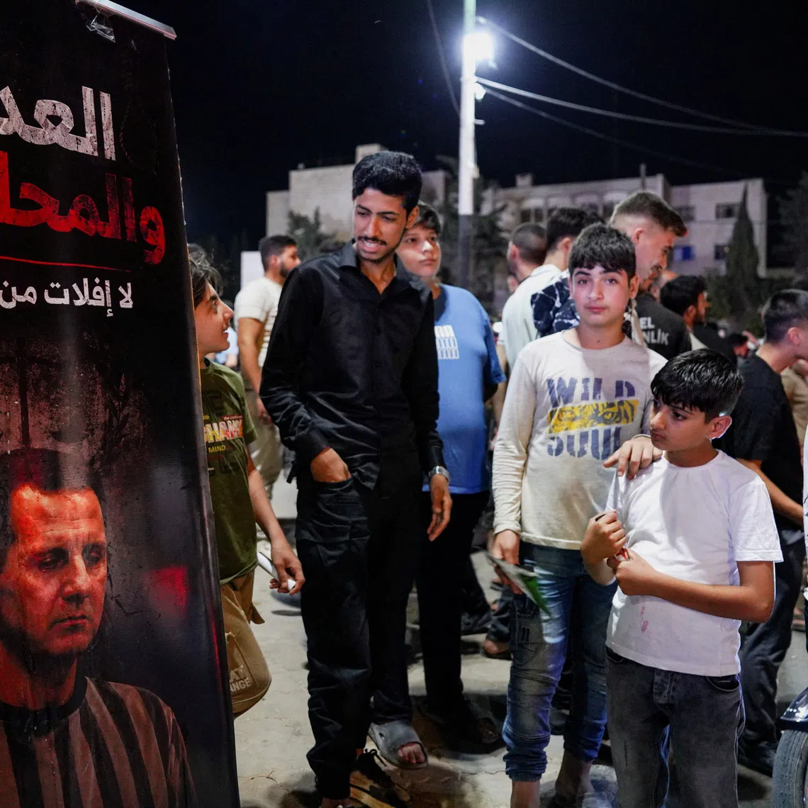 People gather beside a poster depicting ousted President Bashar al-Assad as Syrians celebrate after a Syrian court sentenced Assad and officials who served under his rule to death, in Idlib, Syria, August 11, 2026. REUTERS/Karam al-Masri