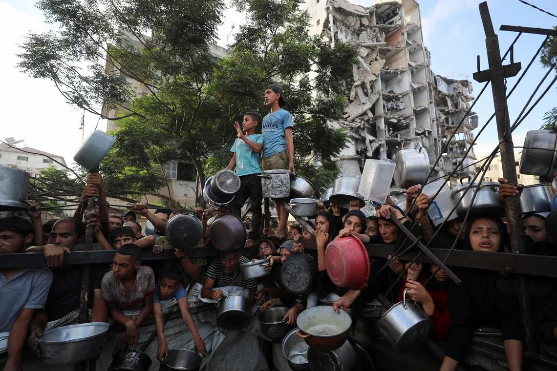 Palestinians wait to receive food from a charity kitchen, amid a hunger crisis, as a destroyed building stands in the background, in Gaza City, July 14, 2025. REUTERS/Mahmoud Issa