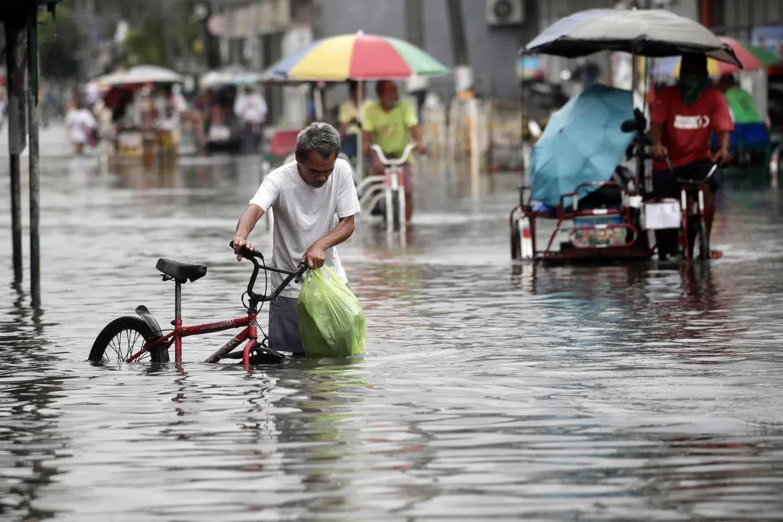 epa10775169 A Filipino man holds a bicycle as he wades through a flooded road in Valenzuela city, Metro Manila, Philippines, 29 July 2023. According to the Philippines’ state weather bureau, Tropical Storm Khanun entered the Philippine Area of Responsibility (PAR) on 29 July as Super Typhoon Doksuri moved out the country leaving more than 30 dead, including dozens on a passenger boat that capsized due to strong winds and waves in Laguna Lake.  EPA-EFE/FRANCIS R. MALASIG