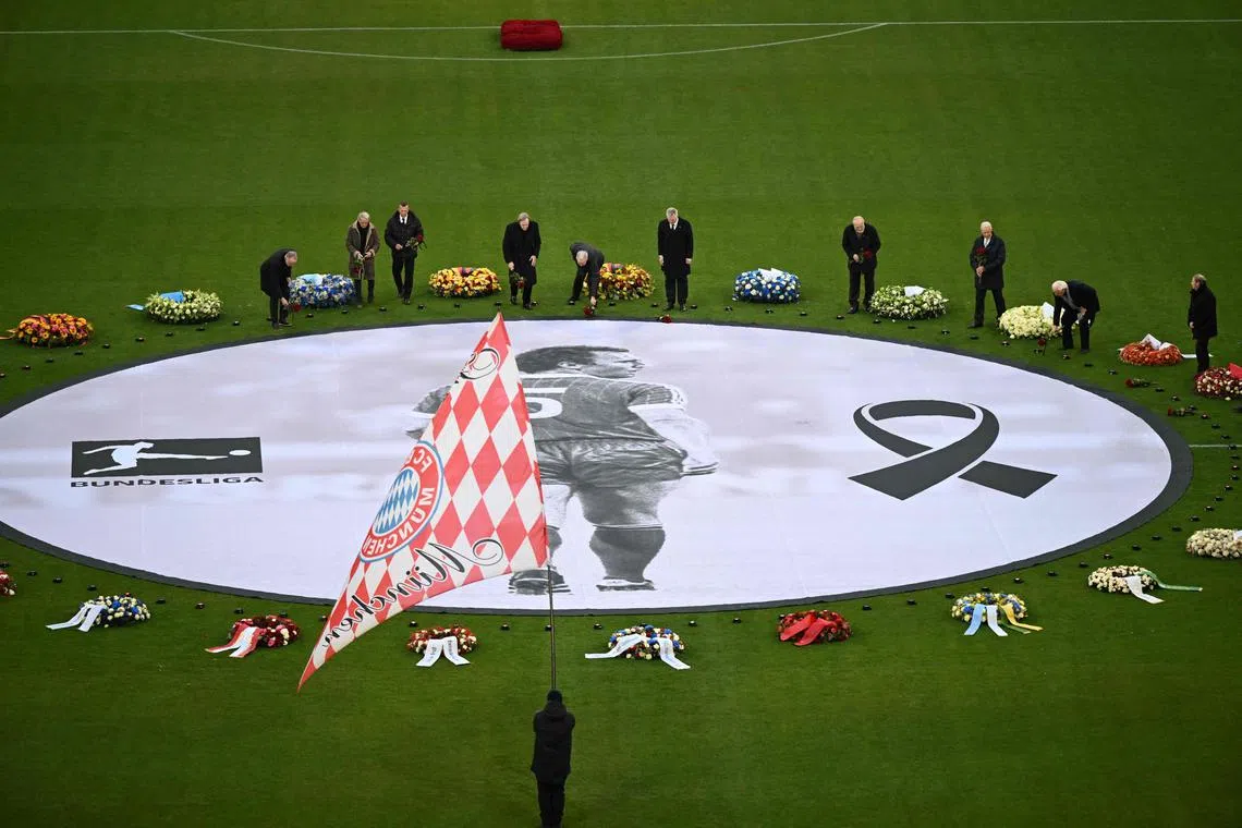 Former German football players place flowers next to wreaths of flowers and a picture of German football legend Franz Beckenbauer during a farewell ceremony organised by his historic club Bayern Munich at the Allianz Arena.