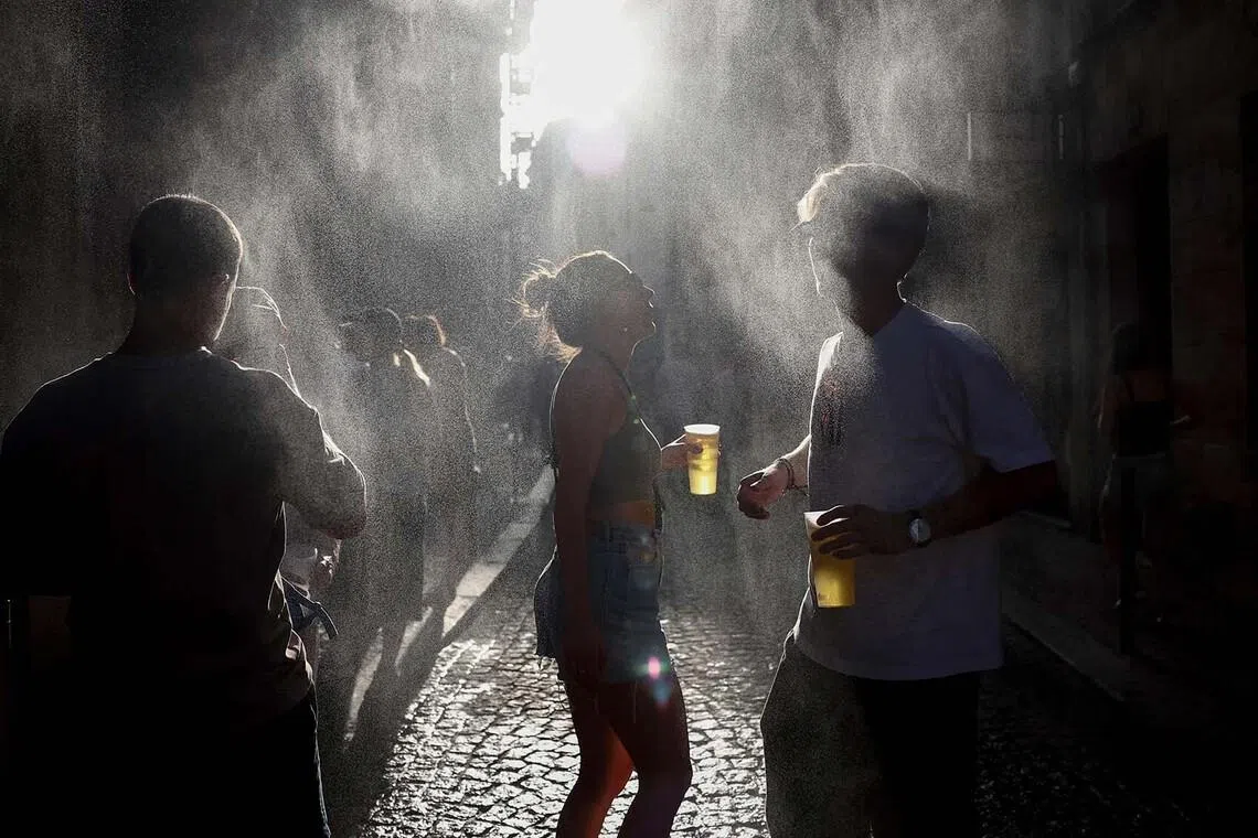 Partygoers cooling off under a mist sprayer as they dance and drink in a street while taking part in the annual street music festival, Fete De La Musique, during a heatwave in Bordeaux, southwestern France on June 21.