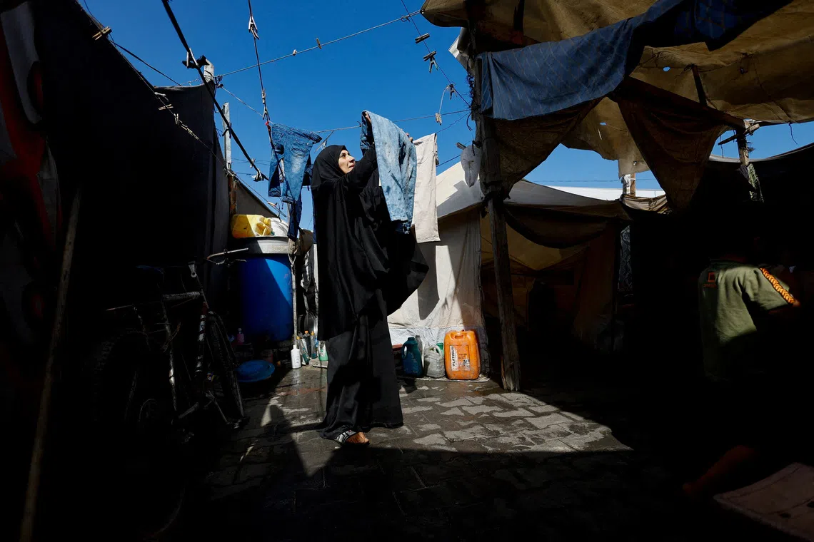 A displaced Palestinian woman hanging laundry as she takes shelter in a tent, after fleeing her home due to the Israeli military offensive, in Nuseirat, central Gaza Strip, on Oct 7, 2025. 