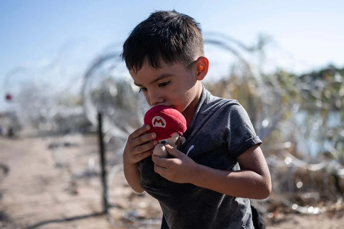 A young migrant from El Salvador kisses a Mario doll before walking to a processing area with his family after crossing the Rio Grande river at the US-Mexico border in Eagle Pass, Texas on Sept 23.