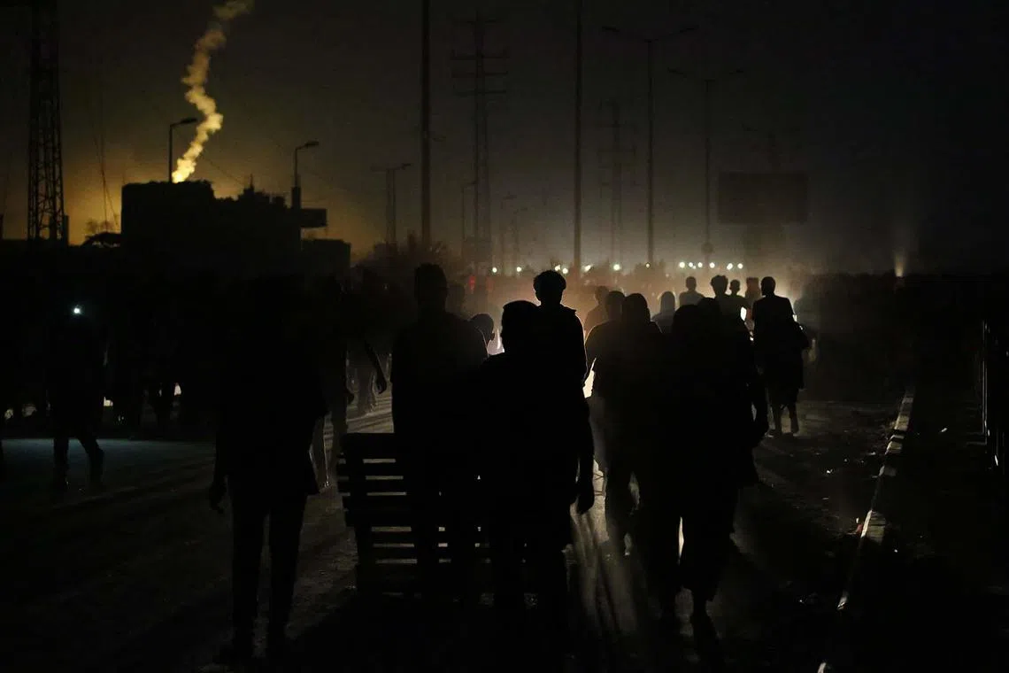 TOPSHOT - Flares light the sky as Palestinians gather to meet trucks carrying humanitarian aid at a distribution point in the Bureij camp for Palestinian refugees in the central Gaza Strip early on June 9, 2025. (Photo by Eyad BABA / AFP)