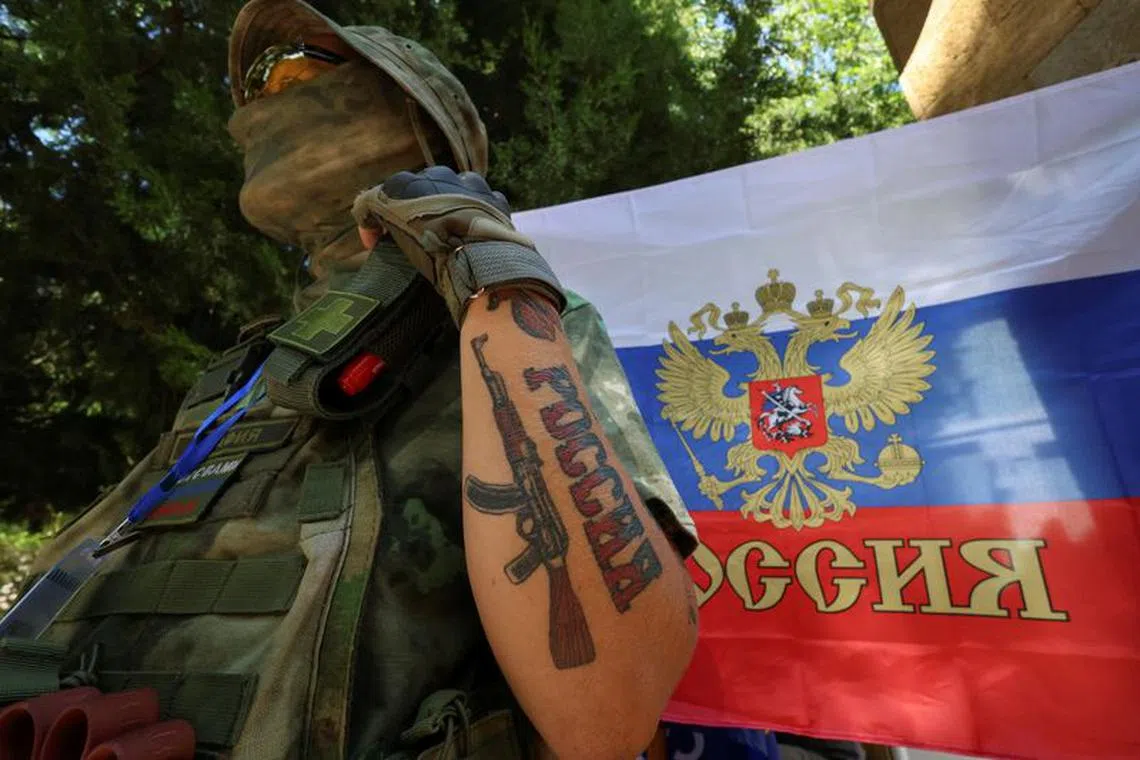 File photo: A participant stands next to a Russian state flag at an exhibition showcasing volunteers' product range, manufactured to supply the needs of service members involved in Russia's military campaign in Ukraine, in Yevpatoriya, Crimea, July 29, 2023. A tattoo reads: \"Russia\". REUTERS/Alexey Pavlishak/File photo
