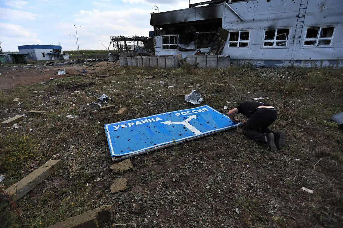 A photo taken during a media tour organised by Ukraine on Aug 16 shows a man examining a damaged road sign with directions to Ukraine and Russia, at a destroyed border crossing.