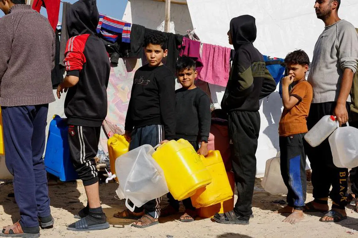 Boys hold containers while they line up, as displaced Palestinians, who fled their houses due to Israeli strikes, shelter in a tent camp near the border with Egypt, amid the ongoing conflict between Israel and the Palestinian Islamist group Hamas, in Rafah in the southern Gaza Strip, December 11, 2023. REUTERS/Mohammed Salem