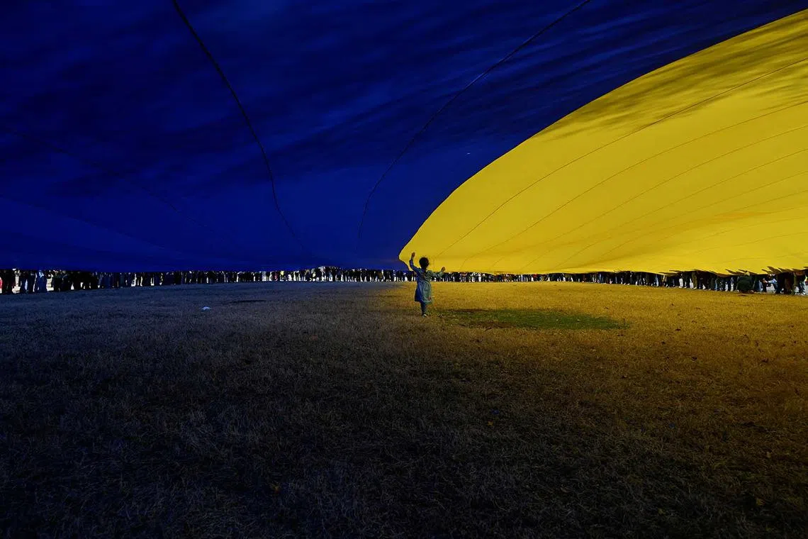 Haley Romero, 6, standing beneath a massive Ukrainian flag held by demonstrators as they rally in support of Ukraine during a protest near the White House in Washington, DC, US, March 8, 2025. 
