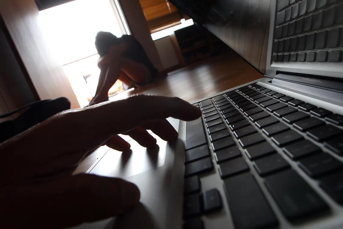 Posed photo of a person crouching in a corner in desolation and another using a laptop to illustrate a story on online bullying.
