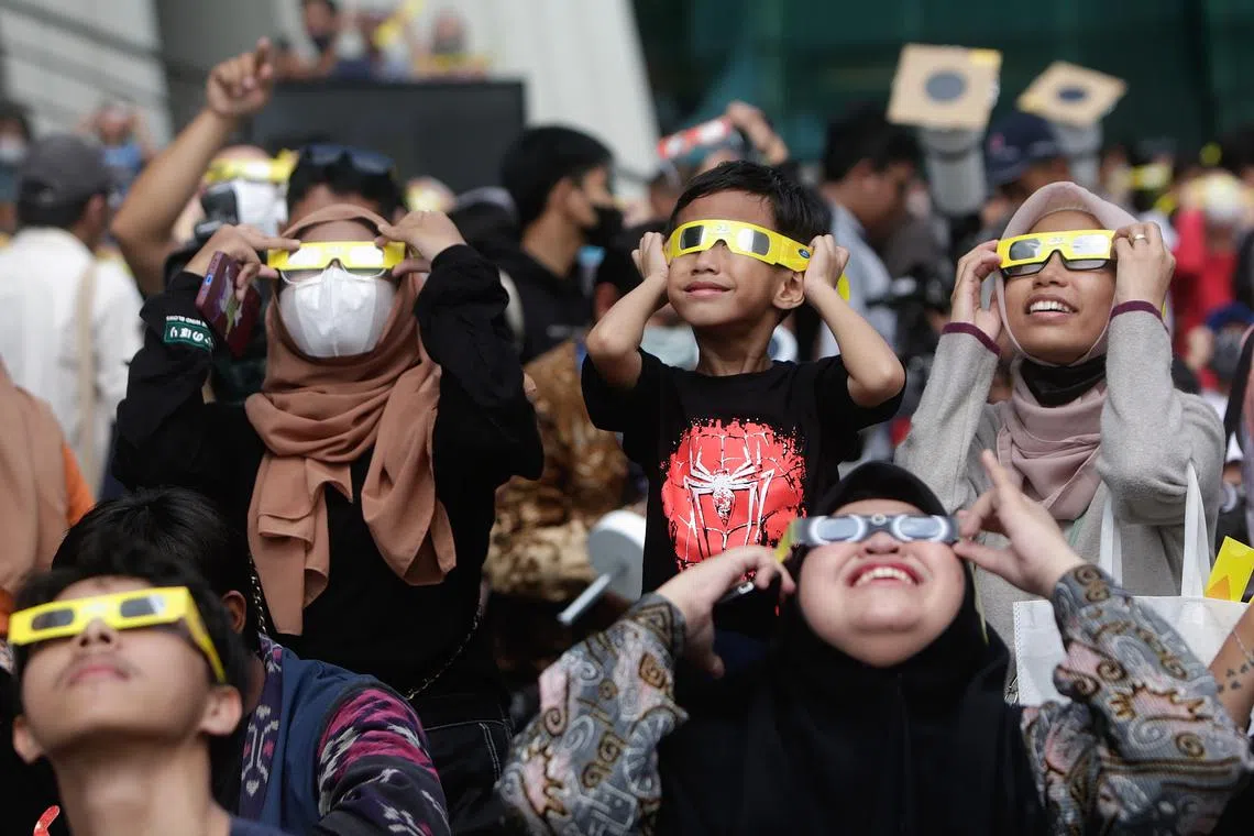 People wearing solar viewing glasses look up at the sun as they watch a solar eclipse at Jakarta Planetarium in Jakarta, Indonesia, April 20, 2023.